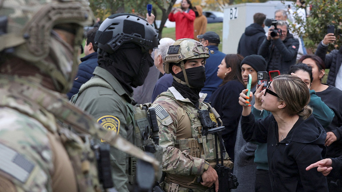 Woman holds her phone up while interacting with federal agents